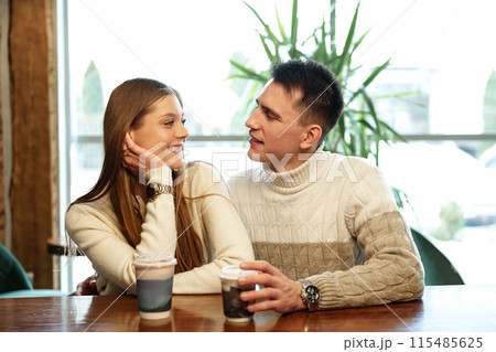 Smiling Couple Enjoying Warm Beverages at a Cozy Cafe on a Sunny Afternoon Smiling Couple Enjoying Warm Beverages at a Cozy Cafe on a Sunny Afternoon 115485625