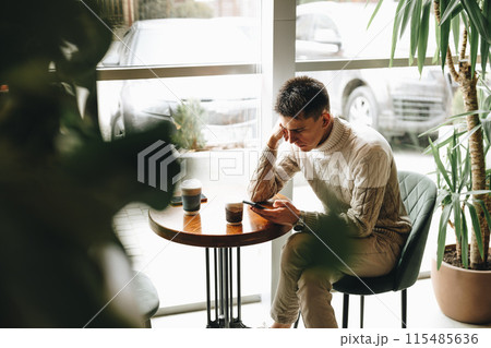 Young Man Engrossed in Smartphone at a Modern Cafe During Daytime 115485636