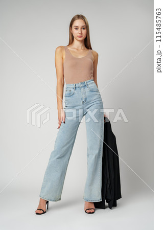 Young Woman Wearing High Rise Jeans and Tank Top posing on gray background in studio 115485763