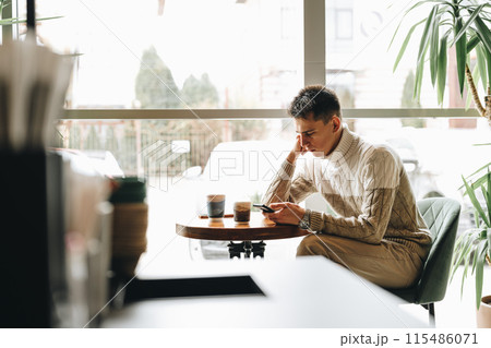 Young Man Engrossed in Smartphone at a Modern Cafe During Daytime 115486071
