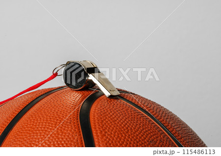Close-Up View of a Whistle Resting on a Basketball Against a Grey Background 115486113