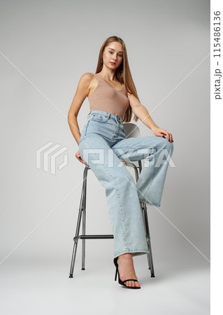Young Woman Sitting on Stool in High Rise Jeans on gray background Young Woman Sitting on Stool in High Rise Jeans on gray background 115486136