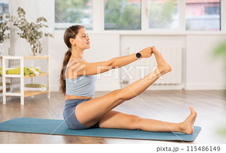 Sportive girl practicing seated hand to toe pose of yoga in light room 115486149