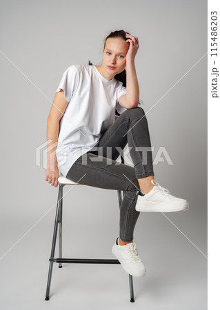 Curly girl model posing on a chair against gray background 115486203