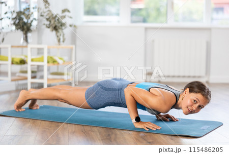 Young girl maintaining low plank position in sunlit room 115486205