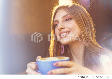 Portrait of a young woman having a cup of coffee and looking through the window 115486208