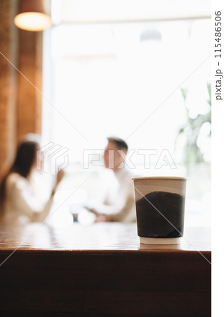 Two People Engage in Conversation Behind Coffee Cup on Wooden Table Two People Engage in Conversation Behind Coffee Cup on Wooden Table 115486506