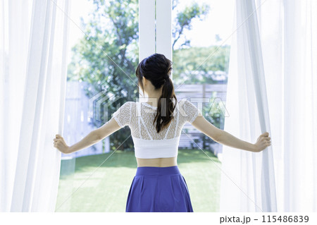 レースのカーテンを開ける若い女性の後姿 115486839