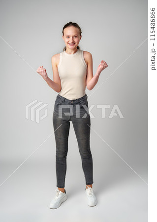 Young Woman in Casual Attire Smiling and Making a Fist Pump Gesture on a Plain Background Young Woman in Casual Attire Smiling and Making a Fist Pump Gesture on a Plain Background 115486866