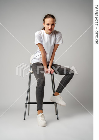 Curly girl model posing on a chair against gray background 115486891