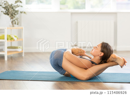 Sportive girl practicing complex pose of yoga in light room 115486926