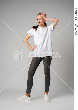 Beautiful young girl posing in white T-shirt and jeans on gray background Beautiful young girl posing in white T-shirt and jeans on gray background 115487122