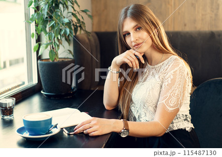 Young business woman sitting at the table in a coffee shop and making notes 115487130