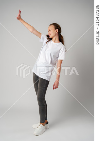 Beautiful young girl posing in white T-shirt and jeans on gray background 115487286