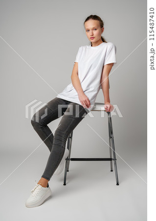 Curly girl model posing on a chair against gray background Curly girl model posing on a chair against gray background 115487410