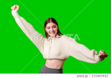 Joyful Young Woman Celebrates With Arms Raised Against Green Screen Joyful Young Woman Celebrates With Arms Raised Against Green Screen 115487652