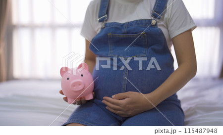 A portrait of happy Asian pregnant woman save financial money for baby with piggy bank in bedroom at home. Having a baby. Family people lifestyle. Mom love. A portrait of happy Asian pregnant woman save financial money for baby with piggy bank in bedroom at home. Having a baby. Family people lifestyle. Mom love. 115487948