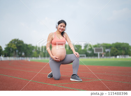 A portrait of happy Asian pregnant woman running on rubber floor, track on a sports stadium. Sport and recreation background. Having a baby. Family people lifestyle. Mom lifestyle. 115488396