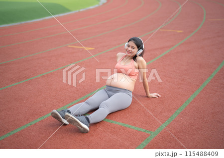 A portrait of happy Asian pregnant woman running on rubber floor, track on a sports stadium. Sport and recreation background. Having a baby. Family people lifestyle. Mom lifestyle. 115488409