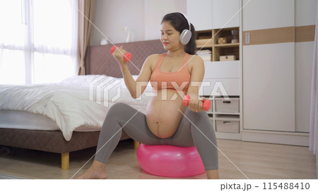 A portrait of happy Asian pregnant woman in bedroom at home. Having a baby. Training workout. Exercise indoor with sport equipment. Athletic. Family people lifestyle. Mom love. Recreation. 115488410