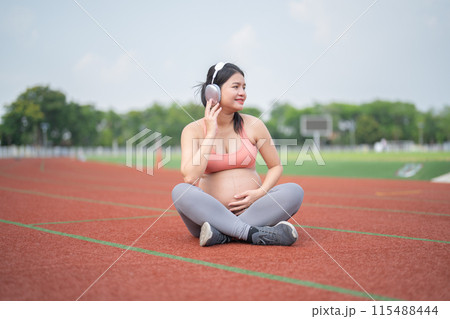 A portrait of happy Asian pregnant woman running on rubber floor, track on a sports stadium. Sport and recreation background. Having a baby. Family people lifestyle. Mom lifestyle. A portrait of happy Asian pregnant woman running on rubber floor, track on a sports stadium. Sport and recreation background. Having a baby. Family people lifestyle. Mom lifestyle. 115488444