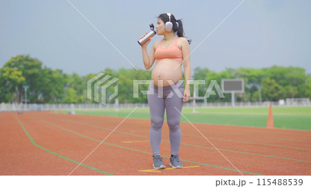 A portrait of happy Asian pregnant woman running on rubber floor, track on a sports stadium. Sport and recreation background. Having a baby. Family people lifestyle. Mom lifestyle. 115488539