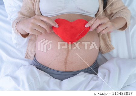 A Portrait of happy Asian pregnant woman with heart in bedroom at home. Having a baby. Family people lifestyle. Love. A Portrait of happy Asian pregnant woman with heart in bedroom at home. Having a baby. Family people lifestyle. Love. 115488817