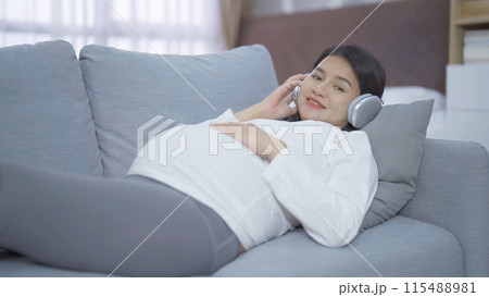 A Portrait of happy Asian pregnant woman listening to music with headphones in bedroom at home. Having a baby. Family people lifestyle. Love. A Portrait of happy Asian pregnant woman listening to music with headphones in bedroom at home. Having a baby. Family people lifestyle. Love. 115488981