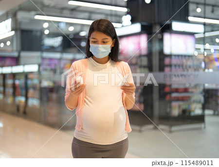 A portrait of happy Asian pregnant woman customer walking along supermarket, buying items on grocery products shelves with basket. Food shopping. Having a baby. Family people lifestyle. Mom. 115489011