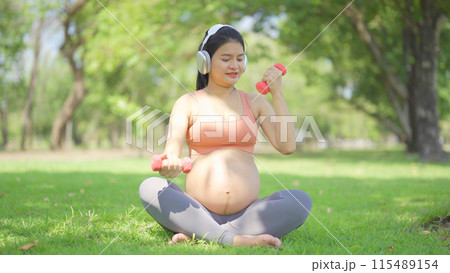 A portrait of happy Asian pregnant woman in yoga class club doing exercise at public garden park. Outdoor sport and recreation. activity with nature trees view. Having a baby. Family people lifestyle. 115489154