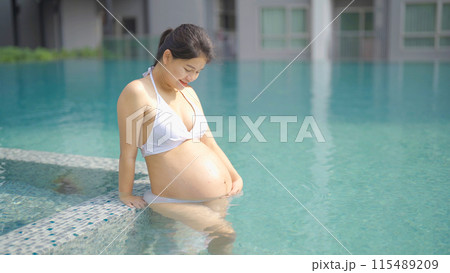 A portrait of happy Asian pregnant woman by the swimming pool. People lifestyle in travel holiday vacation concept. Relaxation. Having a baby. Family people lifestyle. Mom love. A portrait of happy Asian pregnant woman by the swimming pool. People lifestyle in travel holiday vacation concept. Relaxation. Having a baby. Family people lifestyle. Mom love. 115489209