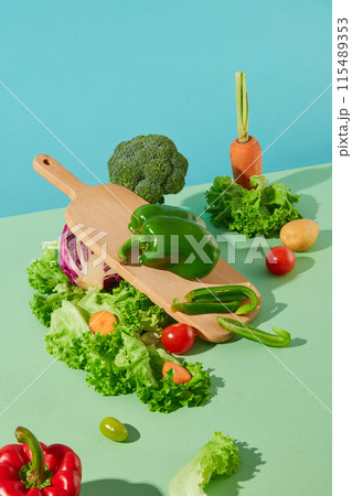 Advertising photo of products has organic ingredients against blue background. Vegetables scattered lay on green table top with a wooden chopping board decoration, blank space for text Advertising photo of products has organic ingredients against blue background. Vegetables scattered lay on green table top with a wooden chopping board decoration, blank space for text 115489353