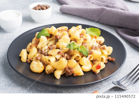 Stewed pasta with minced beef and vegetables, macaroni in Navy style on a plate. grey concrete background. Stewed pasta with minced beef and vegetables, macaroni in Navy style on a plate. grey concrete background. 115490572