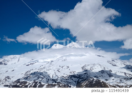 Mountain Elbrus. Against the background of a blue sky with clouds. Russia. Caucasus Mountains. Landscape of snow-capped mountains. Hiking, vacation in the mountains Mountain Elbrus. Against the background of a blue sky with clouds. Russia. Caucasus Mountains. Landscape of snow-capped mountains. Hiking, vacation in the mountains 115491439