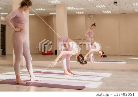 Well looking middle aged sporty woman, fitness instructor in pink sportswear doing stretching and pilates on yoga mat in the studio with mirror. Female fitness yoga. Healthy lifestyle and harmony. 115492051