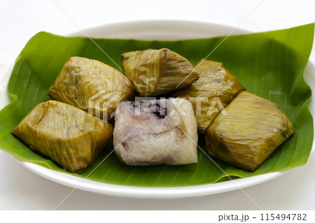 Bundled boiled sticky rice with banana and black beans wrapped in banana leaves 115494782