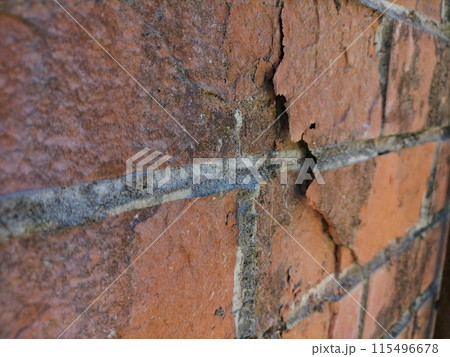 Shattered pieces on a red mud brick wall with deep cracks. Damage to the building structure under the influence of external influences, consequences, destruction, is subject to restoration. Shattered pieces on a red mud brick wall with deep cracks. Damage to the building structure under the influence of external influences, consequences, destruction, is subject to restoration. 115496678