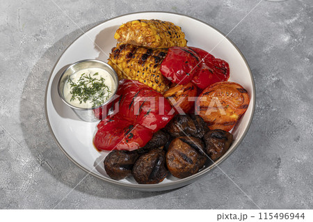 Grilled vegetables on a plate, corn and bell peppers, mushrooms and sauce. 115496944