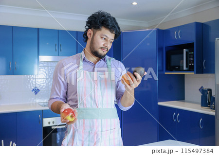 リンゴとアボガドを持って悩むエプロンを着た男性 リンゴとアボガドを持って悩むエプロンを着た男性 115497384