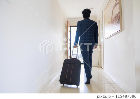 キャリーケースを持ち玄関に向かうスーツの男性の後ろ姿 115497396