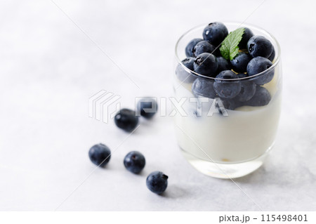 Ripe organic blueberries with yogurt in a glass on white stone table background. Selective focus. Ripe organic blueberries with yogurt in a glass on white stone table background. Selective focus. 115498401
