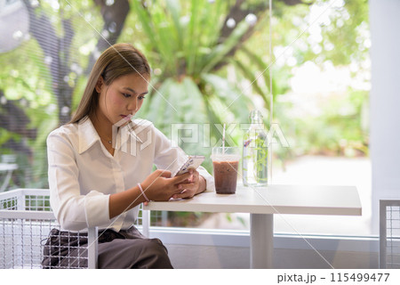 Asian student takes a break at a modern cafe and checking her smartphone Asian student takes a break at a modern cafe and checking her smartphone 115499477