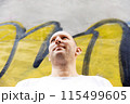 Bald man in white t-shirt looking sideways, colorful graffiti background, urban setting 115499605