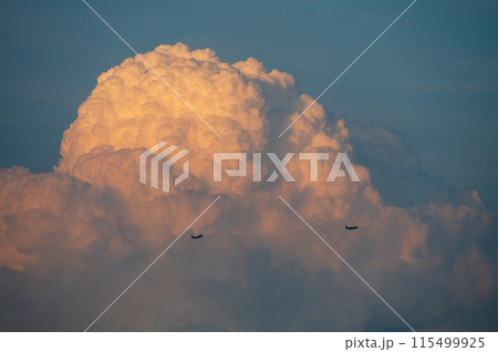夕日に染まる入道雲の前を通る飛行機2機 115499925