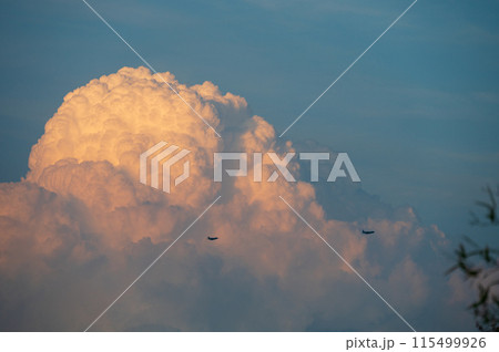 夕日に染まる入道雲の前を通る飛行機2機 115499926