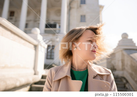 A woman with long hair is standing on a set of stairs. She is wearing a green shirt and a tan coat. A woman with long hair is standing on a set of stairs. She is wearing a green shirt and a tan coat. 115500301