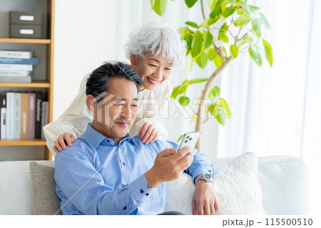 リビングでスマホを見るシニア夫婦 リビングでスマホを見るシニア夫婦 115500510