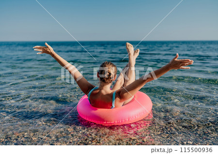 A woman is floating in a pink inflatable raft on a beach 115500936