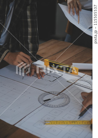 Team of multiethnic architects working on construction plans in meeting room. Engineers discussing on project in office. Mature businessman and woman standing around table working on blueprint. Team of multiethnic architects working on construction plans in meeting room. Engineers discussing on project in office. Mature businessman and woman standing around table working on blueprint. 115505537