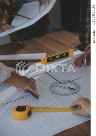 Team of multiethnic architects working on construction plans in meeting room. Engineers discussing on project in office. Mature businessman and woman standing around table working on blueprint. 115505538